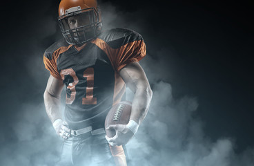 American football player on a dark background in smoke in black and orange equipment.