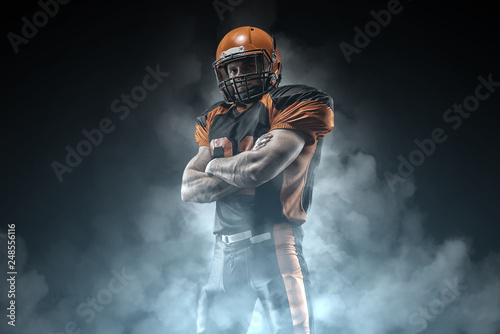 American football player on a dark background in smoke in black and orange equipment.