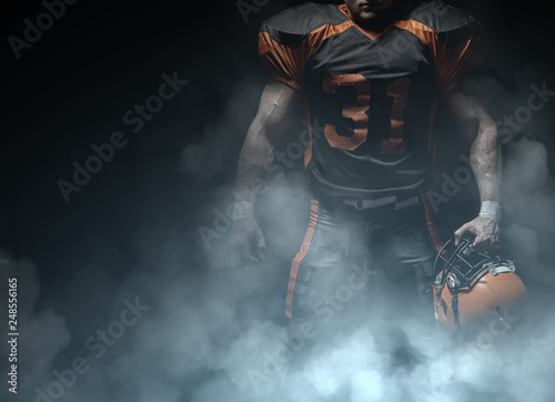 American football player on a dark background in smoke in black and orange equipment.