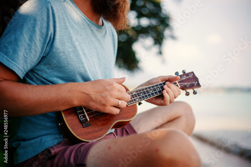 Young handsome redhead man with a beard playing a ukulele on a tropic beach, music, art, travel and vacations concept photo