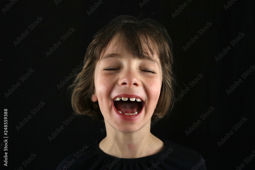Portrait of a young girl laughing out loud with dimples and her eyes closed against a black background Portrait of a young girl laughing out loud with dimples and her eyes closed against a black background