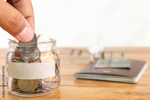 Money savings concept. Collecting money in the money jar for your concept. hand holding coin  Money jar with coins  aircraft toy  and passport.