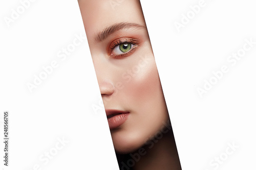 beautiful young woman looking at camera through hole on white © eugenepartyzan