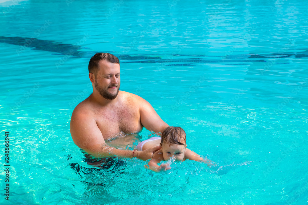 Dad teaches a child to swim in the pool. Father and child having fun in the pool. Dad and daughter swim in the pool on one of the palm trees. Father teaches daughter to swim. The concept of children's