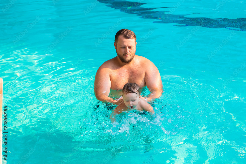 Dad teaches a child to swim in the pool. Father and child having fun in the pool. Dad and daughter swim in the pool on one of the palm trees. Father teaches daughter to swim. The concept of children's