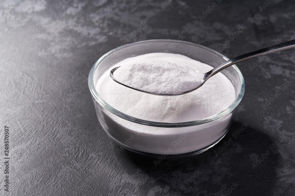 Close-up of baking soda in a  metal spoon on a black background