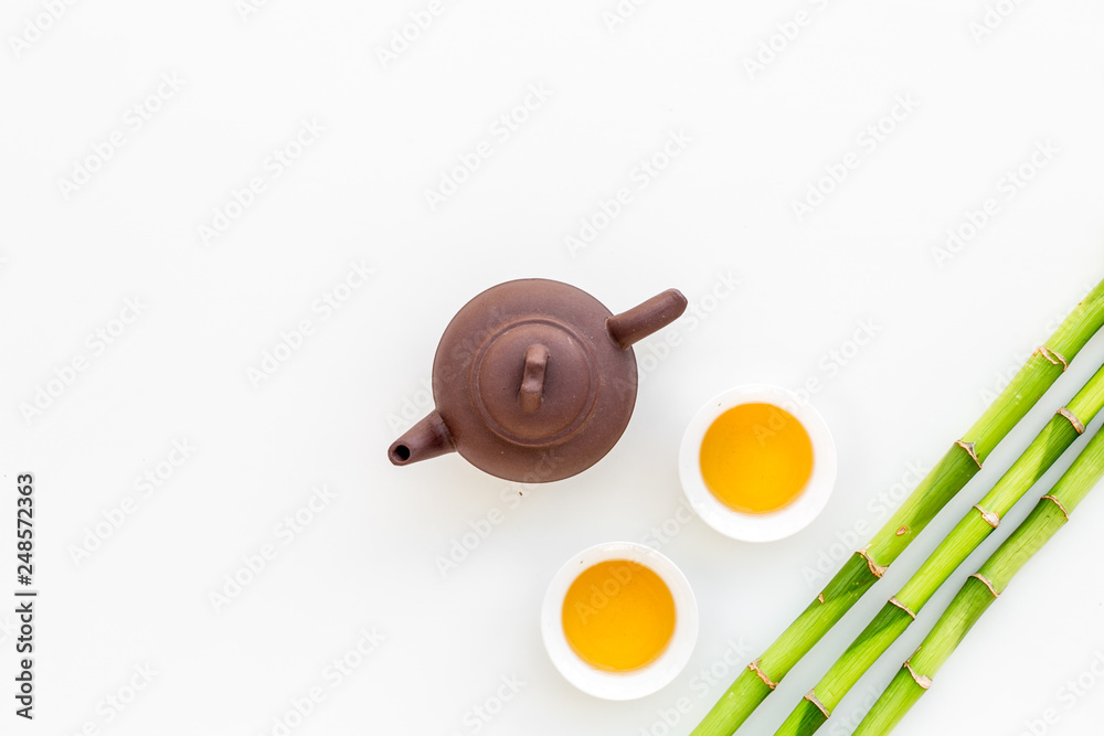 Asian tea traditions. Drink tea. Tea ceremony. Tea pot near cups of green tea and bamboo decoration on white background top view space for text Asian tea traditions. Drink tea. Tea ceremony. Tea pot near cups of green tea and bamboo decoration on white background top view space for text