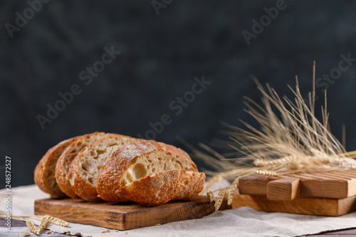 Slices of homemade rye bread on a board and spikelets close-up on a dark background. The concept of healthy food and traditional bakery.