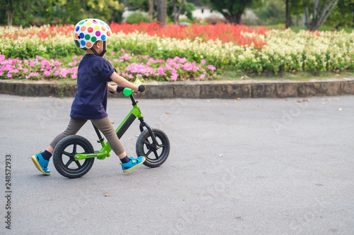 Fototapeta Naklejka Na Ścianę i Meble -  Cute little 2 - 3 years old toddler boy child wearing safety helmet learning to ride first balance bike in sunny summer day, kid cycling at park, Explore & Appreciate Nature with toddlers concept