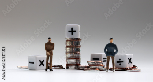 The back of two miniature businessman standing with a pile of coins and arithmetic symbol white cube. photo