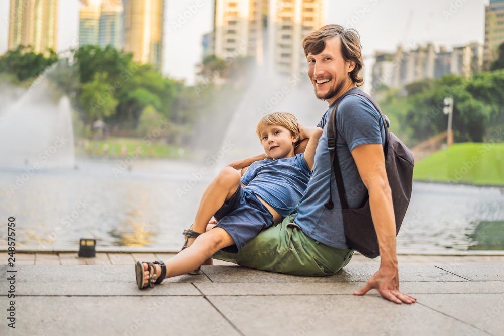 Φωτογραφία Dad and son tourists on background of fountain on the lake at night, near by Twin Towers with city on background