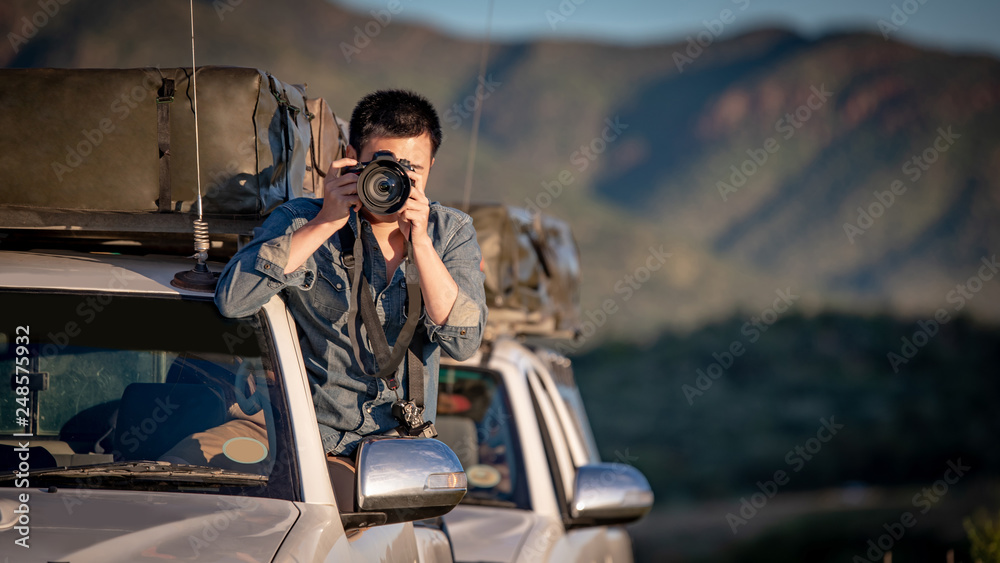 Obraz premium Young Asian man traveler and photographer sitting on the car window taking photo on road trip in Namibia, Africa. Travel photography concept