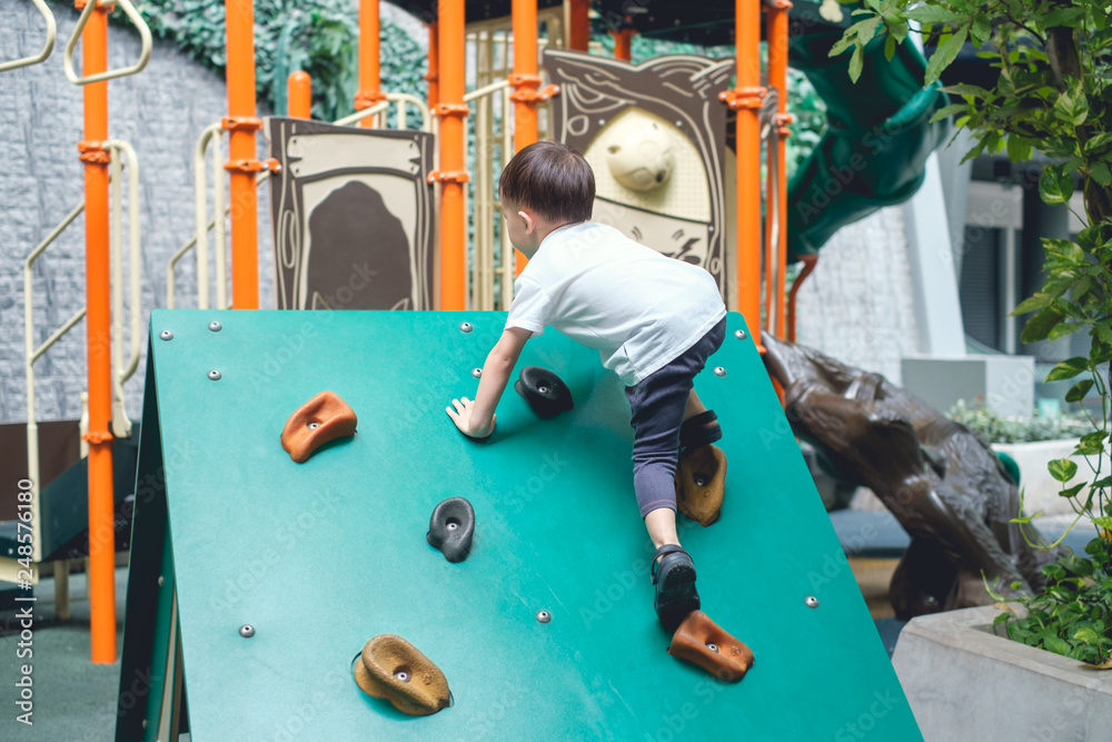 Cute Asian 2 - 3 years old toddler child having fun trying to climb on  artificial boulders