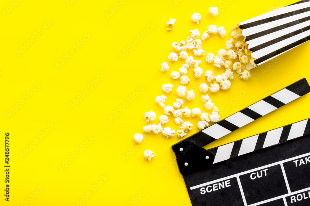 Naklejka premium Movie premiere concept. Clapperboard and popcorn on yellow background top view space for text