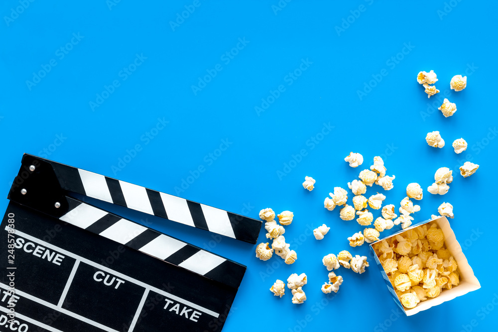 Film watching concept. Clapperboard and popcorn on blue background top view copy space