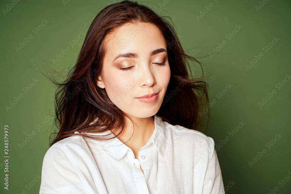 Beauty fashion portrait of sensual closing eyes asian young woman with dark long hair in white shirt on green background Beauty fashion portrait of sensual closing eyes asian young woman with dark long hair in white shirt on green background