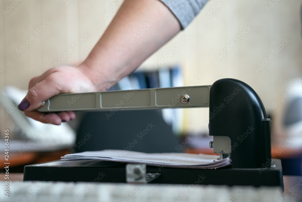 Office worker is punching a paper sheets with hole puncher. Paperwork background. Office worker is punching a paper sheets with hole puncher. Paperwork background.