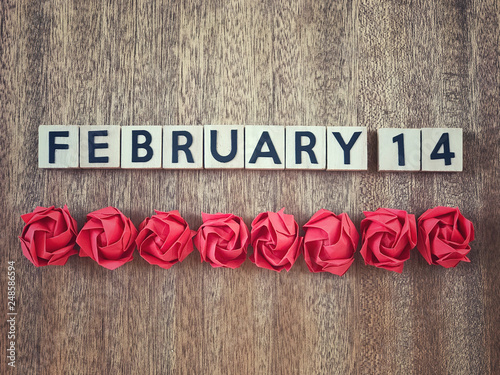 Valentine’s Day concept. February 14 written on wooden blocks and red origami roses on wooden table.