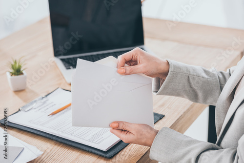cropped view of businesswoman holding envelope at workplace, compensation concept