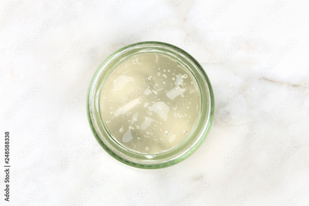 A glass jar with aloe vera gel, shot from above on a white marble background with copy space
