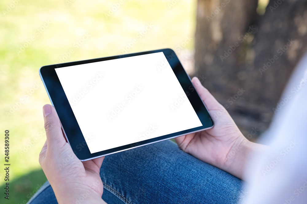 Mockup image of a woman holding and using black tablet pc with blank white desktop screen horizontally while sitting in the outdoors Mockup image of a woman holding and using black tablet pc with blank white desktop screen horizontally while sitting in the outdoors