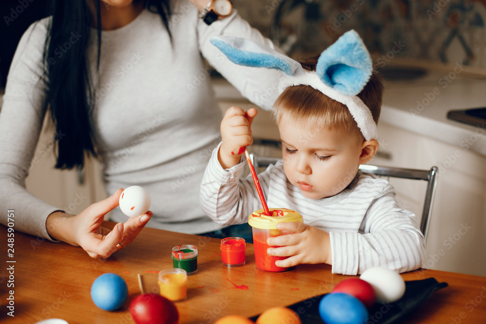 Naklejka premium Mother and son paint eggs. Family sitting in a kitchen. Preparing for Easter