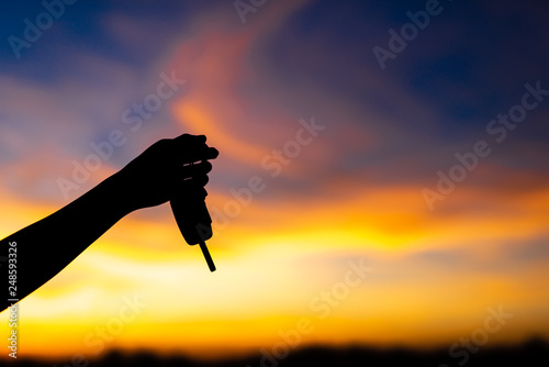 Silhouette hand fo the woman holding car key, beautiful sky in sunset.