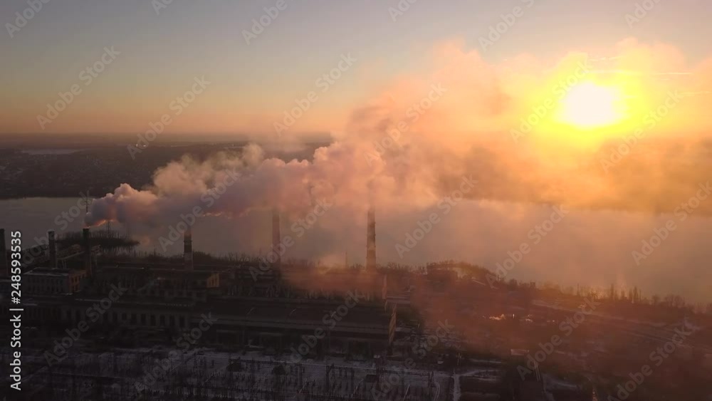 Industrial zone with a large red and white pipe thick white smoke is poured from the factory pipe in contrast to the sun. Industrial zone with a large red and white pipe thick white smoke is poured from the factory pipe in contrast to the sun.
