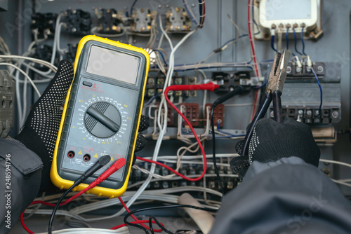 Electrician is checking the voltage in the electrical circuit of the installation with a multimeter. Electric works concept background.