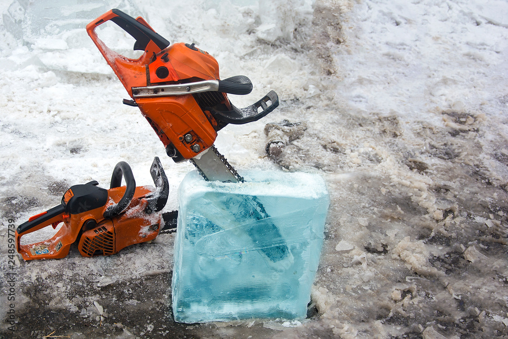 Chainsaw inserted into the ice block. Concept: cutting out figures from ice, folk art, craftsmanship, construction from ice.