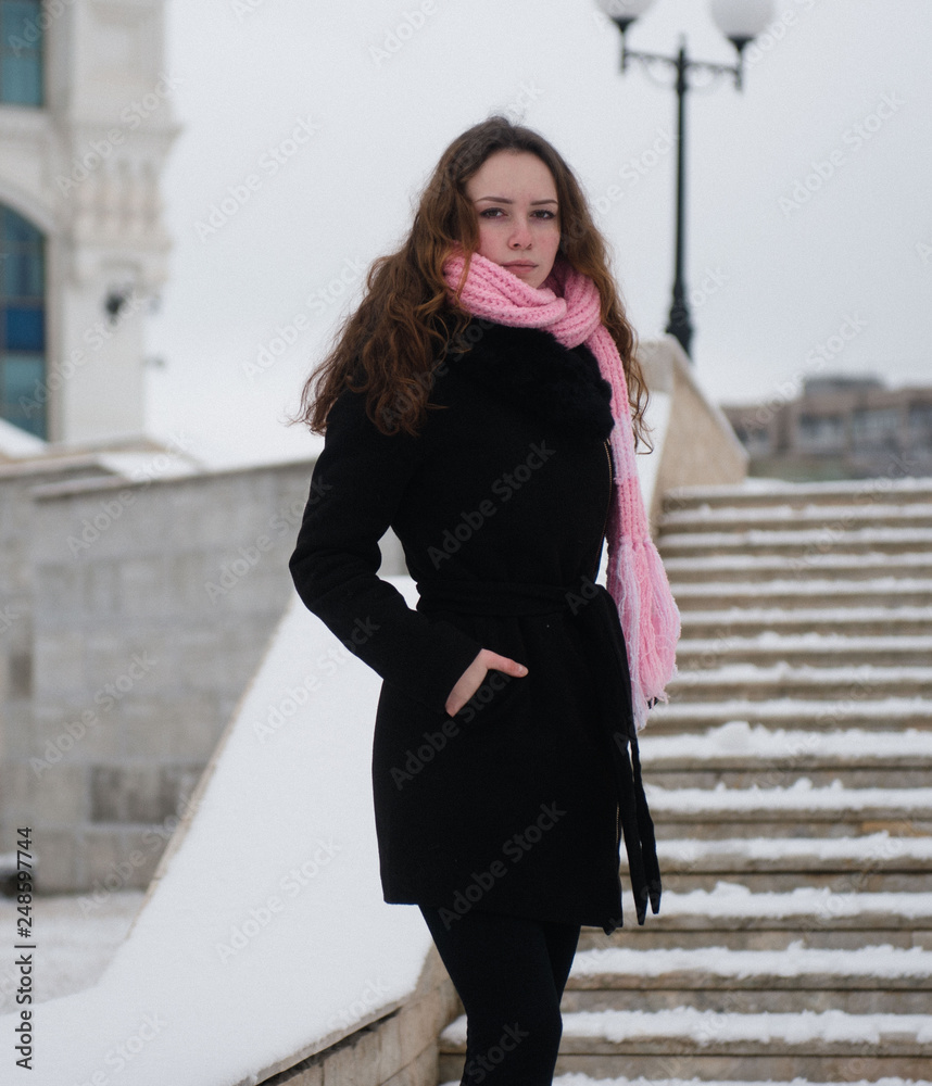 Young woman posing in a black coat and pink woolen scarf in the winter in the park