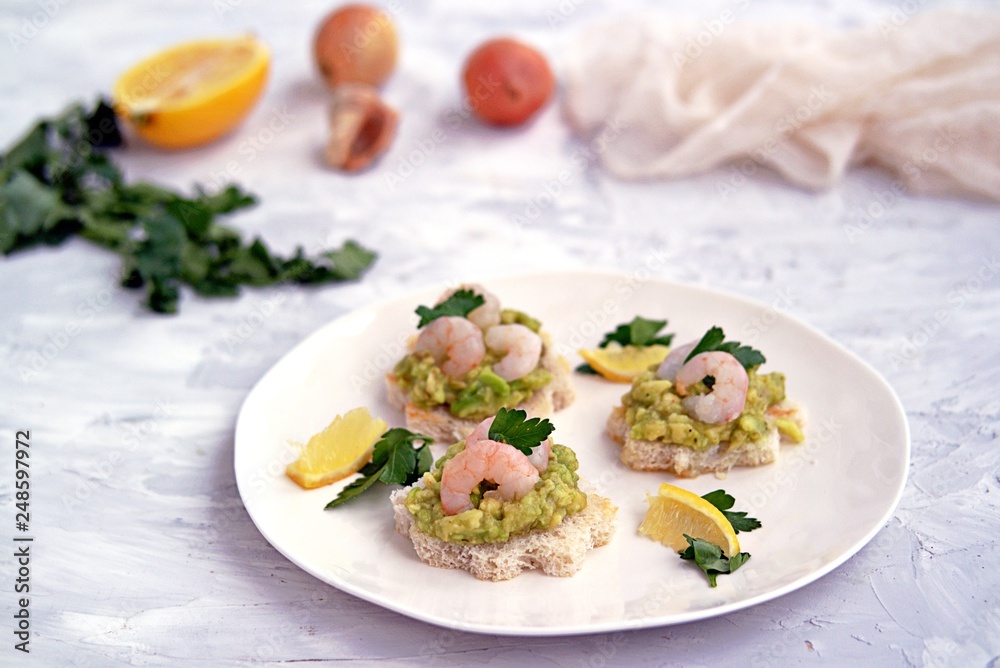 Small snack sandwiches on white bread with guacamole and shrimps on a white plate. Selective focus. Small snack sandwiches on white bread with guacamole and shrimps on a white plate. Selective focus.