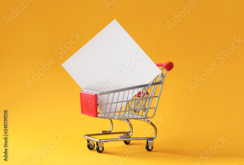 Creative shopping background with shopping cart and empty card in it on yellow background with copy space. Black friday or sale minimal concept mockup.