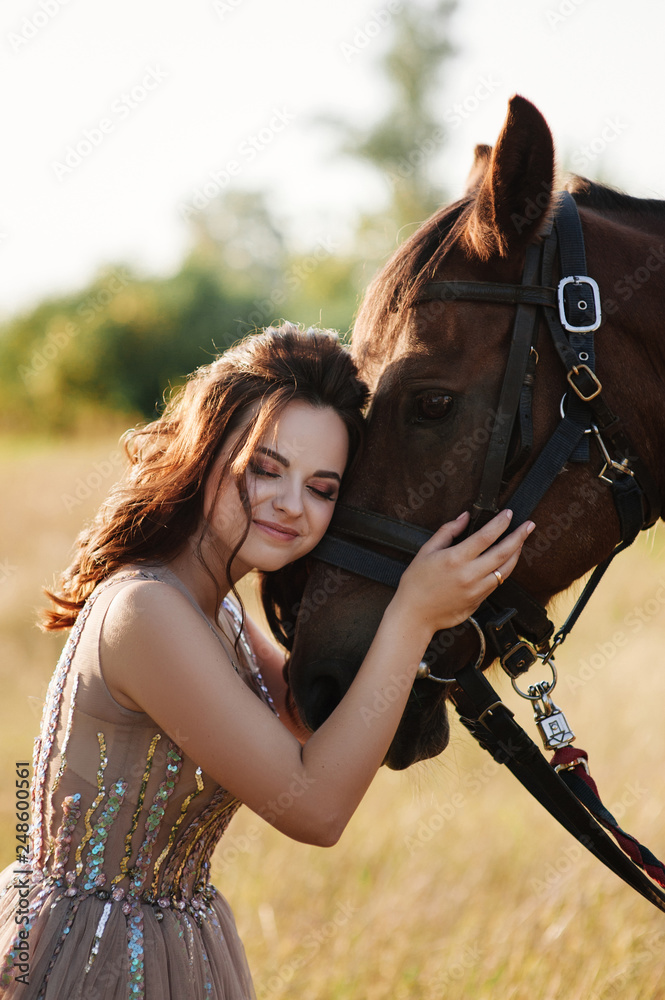 Obraz premium The bride in a delicate pink dress with paillettes on a brown horse. Wedding in the forest at sunset. Walking in the nature near the water.