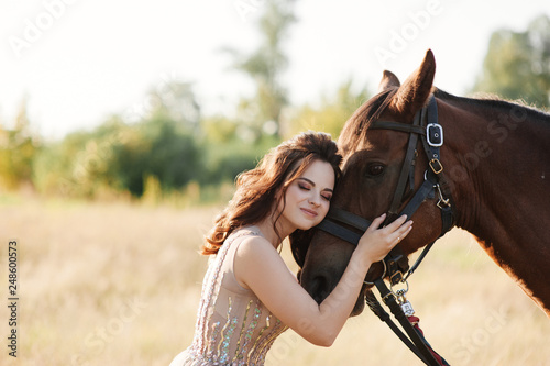 The bride in a delicate pink dress with paillettes on a brown horse. Wedding in the forest at sunset. Walking in the nature near the water.