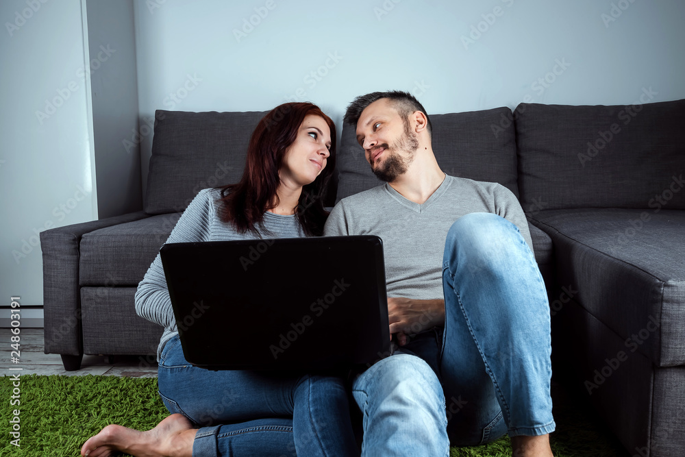 Portrait of a beautiful young couple looking at the camera, against a gray sofa.