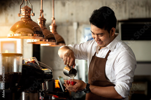 Happy Asian barista pouring milk into red coffee cup for latte art. photo