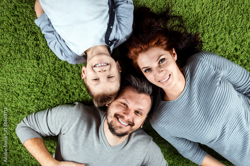 Top view, happy family, dad mom and son are smiling lying on a green carpet. The concept of family, family relationships, happiness, joy. Top view, happy family, dad mom and son are smiling lying on a green carpet. The concept of family, family relationships, happiness, joy.