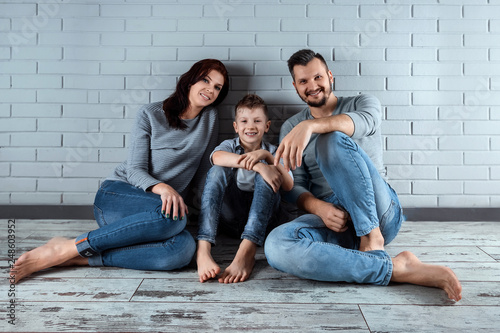 Happy family sitting on the floor against the gray wall. Smiling couple sitting at home. Copy space. The concept of a family, their housing, credit, mortgage.
