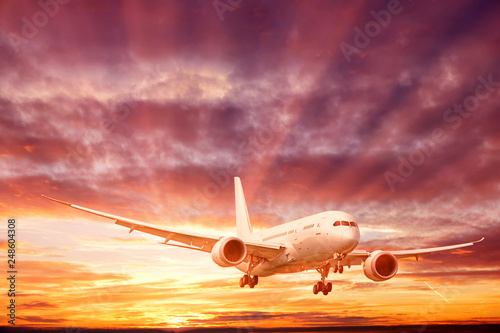 business jet airplane with gear down landing against dramatic sunset sky background corporate air travel commercial airline modern passenger plane aerial front view generic landscape size photo