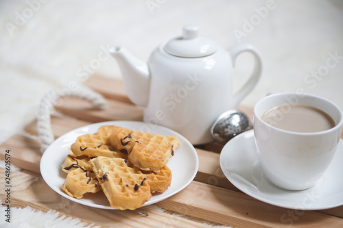 Cozy breakfast in bed, cup of coffee and heart shaped waffles on wooden tray on white and gray cozy blanket, the concept of home comfort, copy space