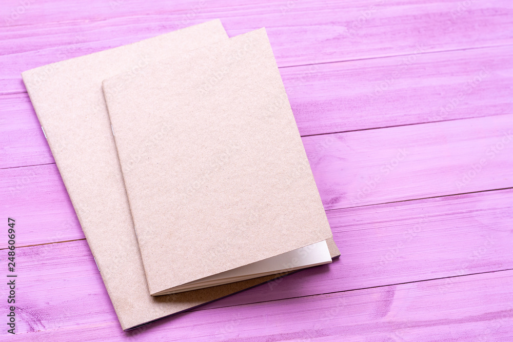 Fototapeta premium Two brown notebook isolated on violet wooden background.