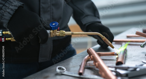 Worker is soldering a pipe by a blow lamp on a factory workbench background. Pipework. photo
