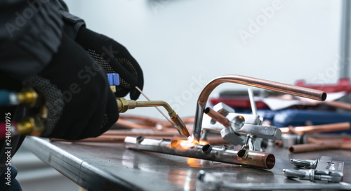 Worker is soldering a pipe by a blow lamp on a factory workbench background. Pipework. photo