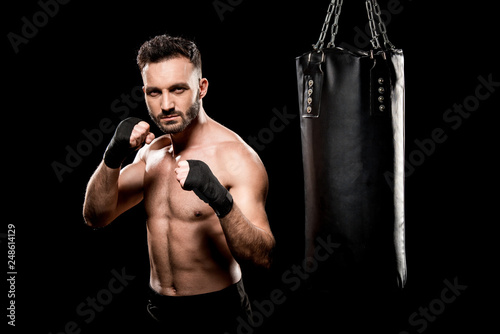muscular boxer kicking punching bag isolated on black