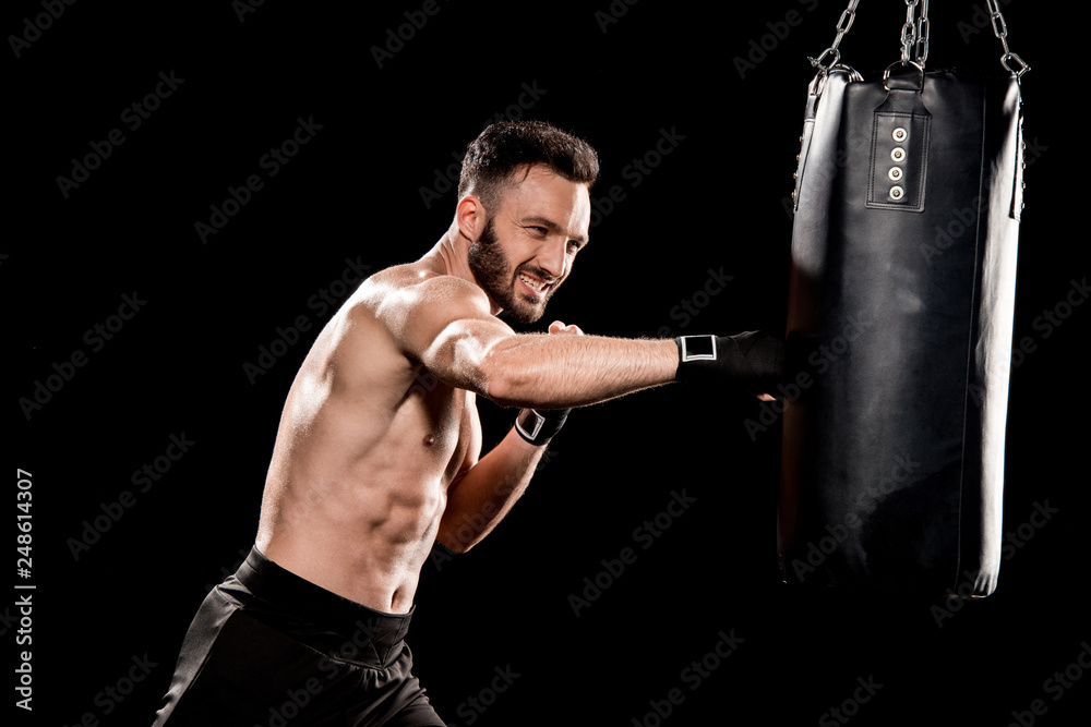 shortless bearded man exercising with punching bag isolated on black