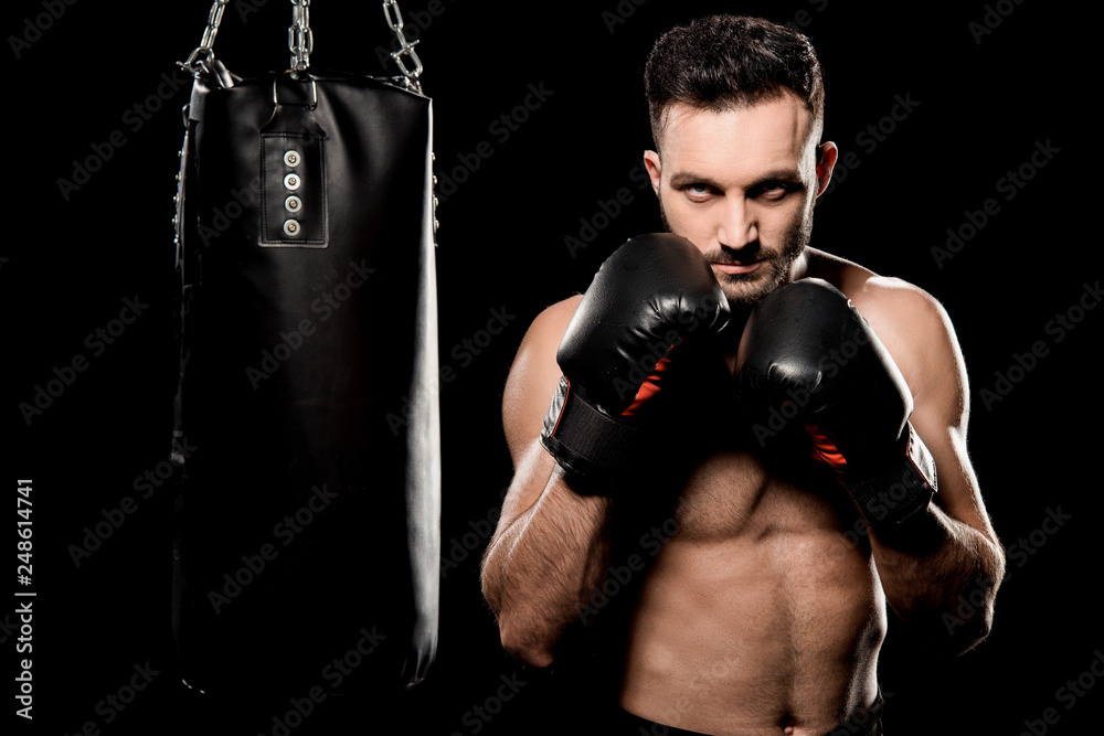 athlete in boxing gloves standing in boxing pose near punching bag isolated on black athlete in boxing gloves standing in boxing pose near punching bag isolated on black