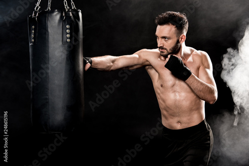 handsome athletic boxer hitting punching bag on black with smoke