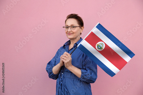 Costa Rica flag. Woman holding Costa Rican flag. Nice portrait of middle aged lady 40 50 years old holding a large flag over pink wall background on the street outdoor. photo