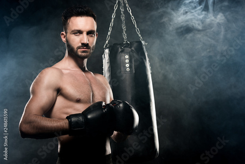 handsome athlete standing in boxing pose on black with smoke